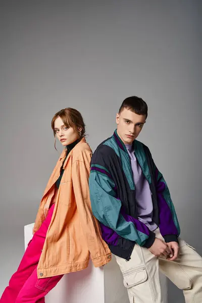 Caring appealing couple in vivid stylish bombers looking at camera on gray backdrop on white cube — Stock Photo