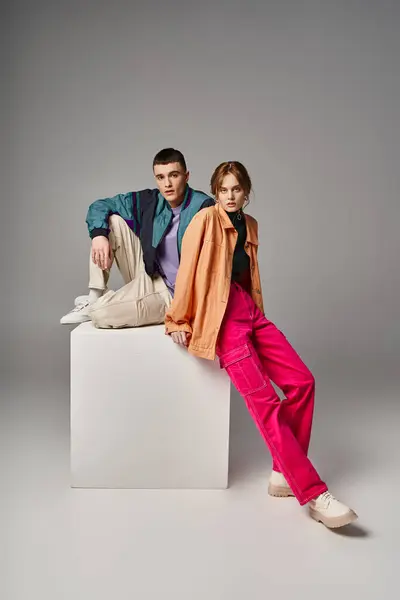 Loving appealing couple in vivid stylish bombers looking at camera on gray backdrop on white cube — Stock Photo