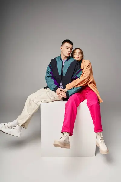 Appealing woman in fashionable bomber looking at camera next to her handsome boyfriend on white cube — Stock Photo