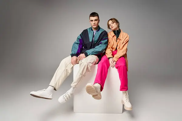 Loving appealing couple in vivid stylish bombers looking at camera on gray backdrop on white cube — Stock Photo