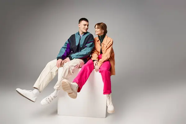 Joyous appealing couple in vibrant trendy bombers looking at each other happily on white cube — Stock Photo