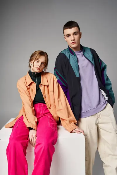 Loving attractive couple in vivid stylish bombers looking at camera on gray backdrop on white cube — Stock Photo