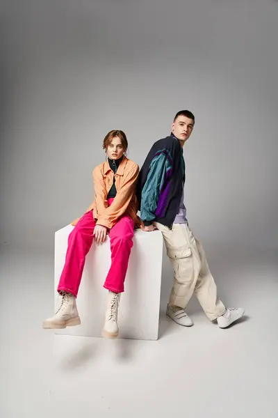 Loving attractive couple in vivid stylish bombers looking at camera on gray backdrop on white cube — Stock Photo