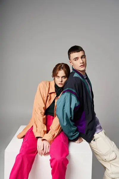 Appealing woman in fashionable bomber looking at camera next to her handsome boyfriend on white cube — Stock Photo