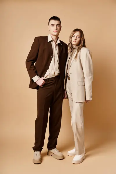 Alluring fashionable couple in stylish suits posing on pastel backdrop and looking at camera — Stock Photo