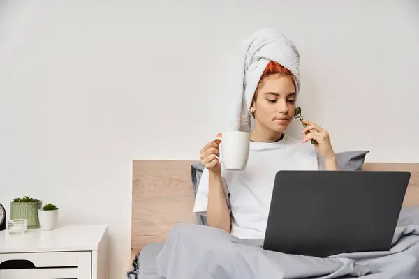 Bella persona queer con asciugamano per capelli utilizzando rullo viso bere tè mentre si guarda film in tv — Foto stock