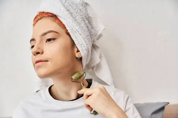 Good looking queer person in comfy homewear with har towel using face roller while at home — Stock Photo