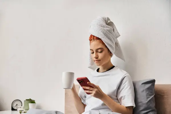 Positive relaxing queer person in homewear with hair towel using phone and drinking tea in bed — Stock Photo