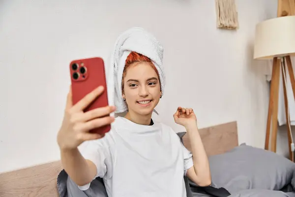 Allegra bella persona queer con asciugamano in biancheria da casa prendendo selfie mentre si rilassa a letto — Foto stock