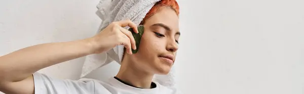 Merry beautiful queer person with hair towel in homewear using gua sha while at home, banner — Stock Photo