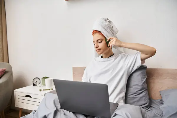 Lustige ziemlich queere Person mit Haartuch Filme auf Laptop und mit gua sha, während im Bett — Stockfoto