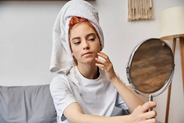 Atractiva persona extravagante con toalla de pelo blanco mirando en el espejo durante la rutina de la mañana en casa - foto de stock