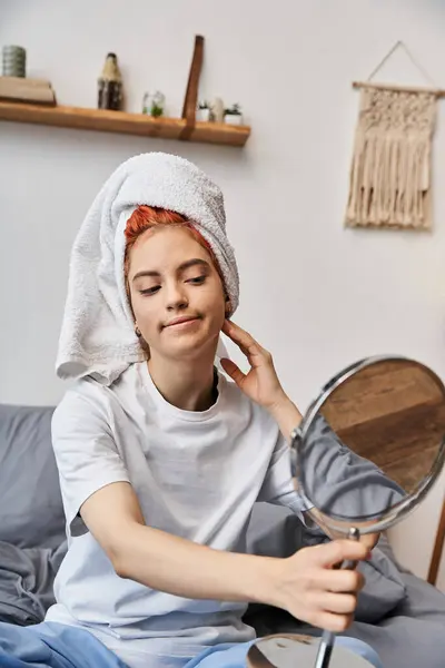 Atractiva persona extravagante con toalla de pelo blanco mirando en el espejo durante la rutina de la mañana en casa - foto de stock