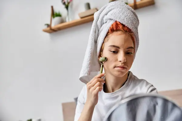 Attractive jolly queer person in homewear using face roller in front of mirror as morning routine — Stock Photo