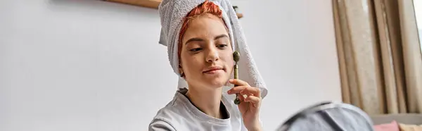 Beautiful queer person in homewear using face roller in front of mirror as morning routine, banner — Stock Photo