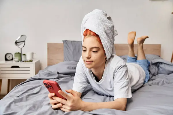 Atraente pessoa extravagante com toalha de cabelo branco olhando para o telefone enquanto relaxa na cama — Fotografia de Stock