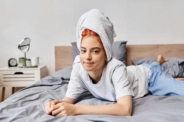 Alegre bela queer pessoa com toalha de cabelo refrigeração em sua cama e sorrindo para a câmera, de manhã — Fotografia de Stock