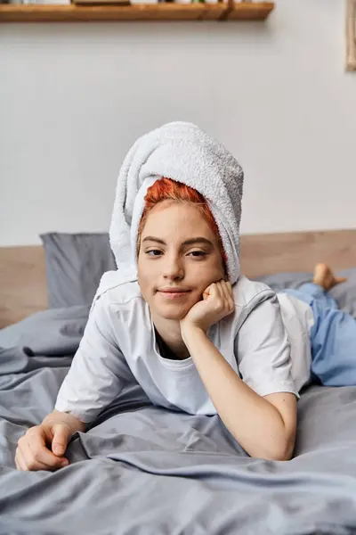 Freudig schöne queere Person mit Haartuch, die in ihrem Bett chillt und in die Kamera lächelt, morgens — Stockfoto