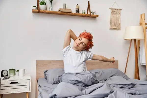 Extravagant young queer person in casual attire waking up and stretching in her bed, leisure time — Stock Photo