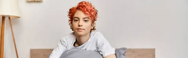 Sonnolenta persona stravagante queer in biancheria da casa con i capelli rossi seduti sul letto guardando la fotocamera, banner — Foto stock