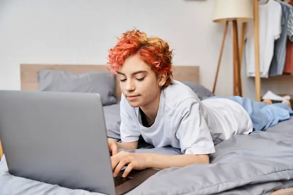 Alegre atraente queer pessoa em aconchegante homewear deitado na cama e surf na internet, lazer — Fotografia de Stock