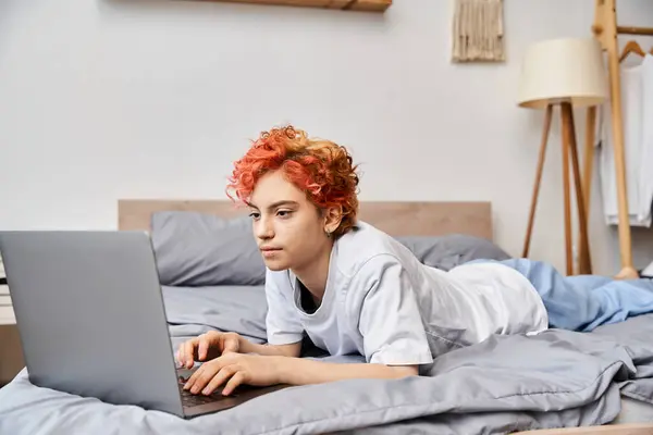 Alegre atraente queer pessoa em aconchegante homewear deitado na cama e surf na internet, lazer — Fotografia de Stock