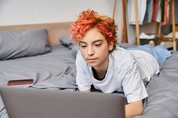 Alegre atractivo queer persona en acogedora ropa de casa acostado en la cama y navegar en Internet, ocio - foto de stock