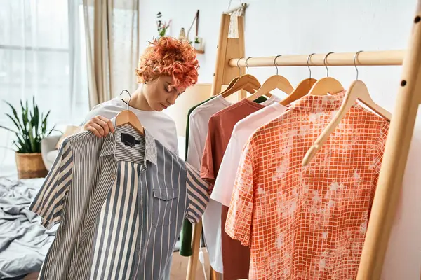 Beautiful red haired extravagant person picking up stylish clothes near rack at home, leisure time — Stock Photo