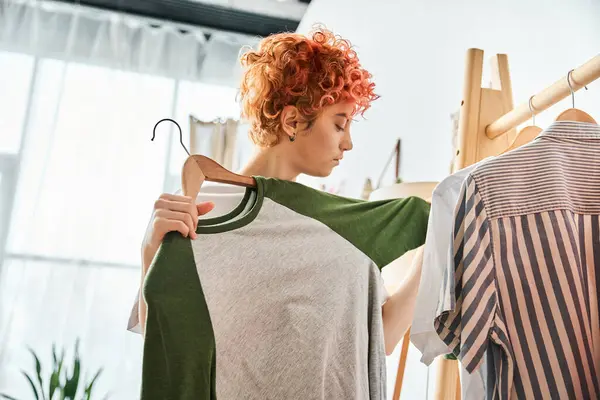 Appealing red haired extravagant person picking up stylish clothes near rack at home, leisure time — Stock Photo