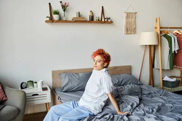 Gut aussehende extravagante Person im weißen T-Shirt mit roten Haaren sitzt auf ihrem Bett, Freizeit — Stockfoto