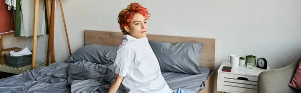 Attractive extravagant person in white t shirt with red hair sitting on bed, leisure time, banner — Stock Photo