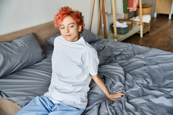 Boa aparência pessoa extravagante em t-shirt branca com cabelo vermelho sentado em sua cama, tempo de lazer — Fotografia de Stock