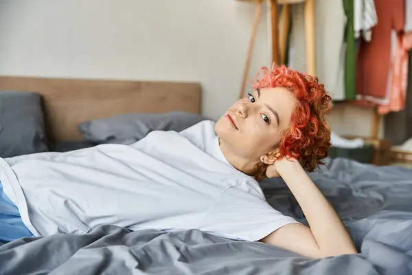 Cheerful appealing queer person with red hair lying on her bed and looking at camera, leisure time — Stock Photo