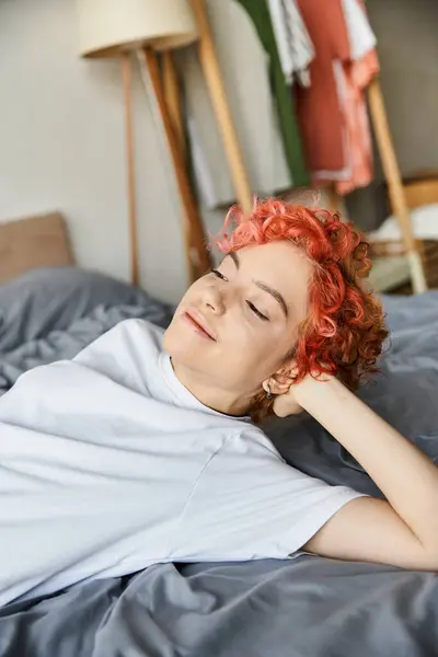 Bela pessoa extravagante com cabelo vermelho vibrante deitado em sua cama e olhando para longe, tempo de lazer — Fotografia de Stock