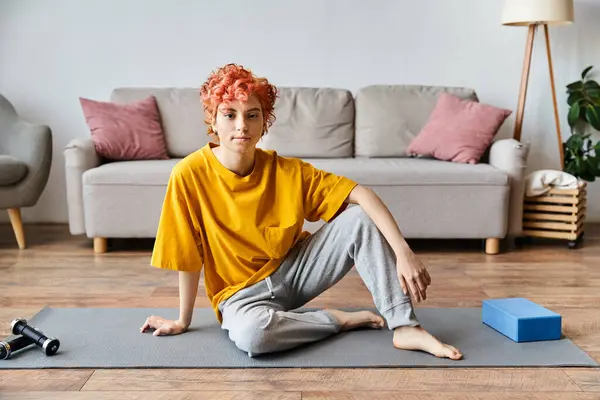Bela pessoa queer em vibrante camiseta amarela sentada no tapete de ioga e olhando para a câmera — Fotografia de Stock