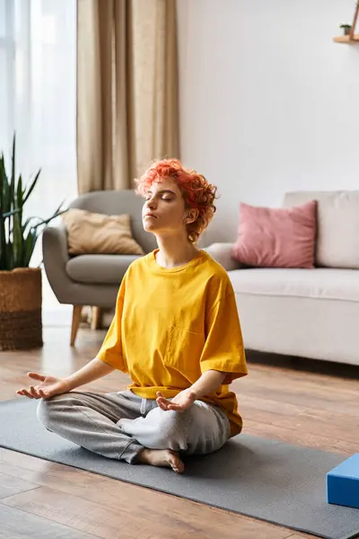 Schöne extravagante queere Person mit roten Haaren in leuchtend gelbem T-Shirt, die zu Hause meditiert — Stockfoto