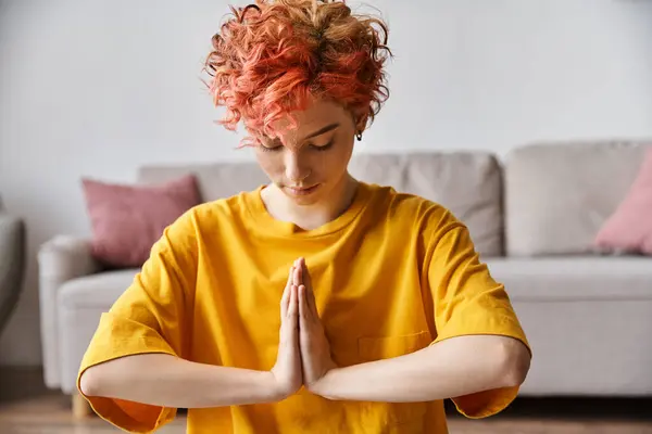 Attraktive extravagante queere Person mit roten Haaren im leuchtend gelben T-Shirt, die zu Hause meditiert — Stockfoto