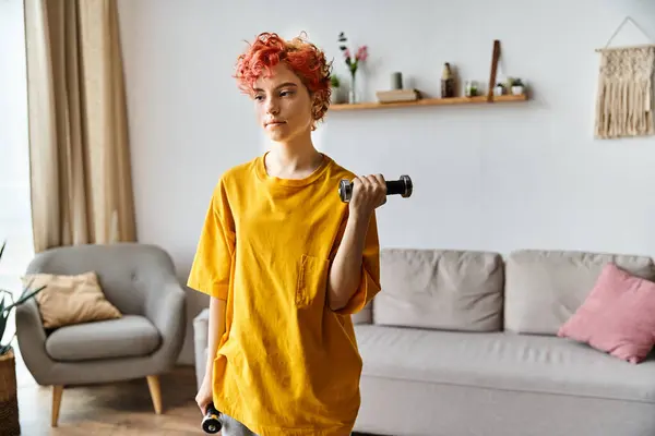 Attractive young queer person in vibrant sport attire exercising with dumbbells while at home — Stock Photo