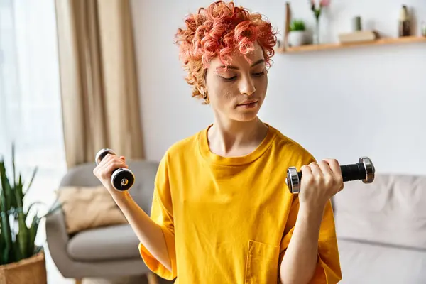Beautiful young queer person in vibrant sport attire exercising with dumbbells while at home — Stock Photo