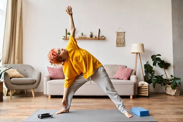 Bien parecido alegre queer persona en casual atuendo ejercitando activamente en yoga mat mientras en casa - foto de stock
