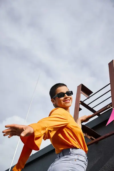 Fröhliche junge Frau in lebendiger Kleidung posiert auf der Treppe auf dem Dach und lächelt glücklich in die Kamera — Stockfoto