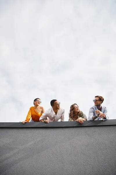 Joyous diverse friends with sunglasses in urban attires posing on roof and smiling at each other — Stock Photo