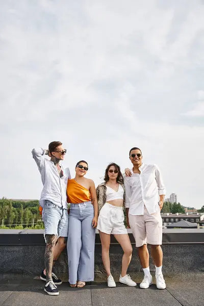 Quattro amici allegri multirazziali con occhiali da sole alla moda in posa gioiosa sul tetto insieme — Foto stock