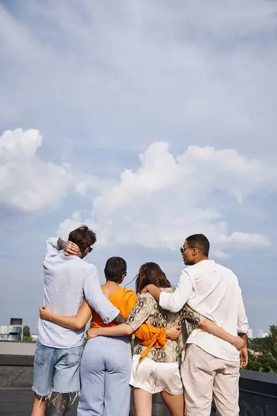 Back view of group of interracial friend in comfy vibrant clothes posing on rooftop together — Stock Photo