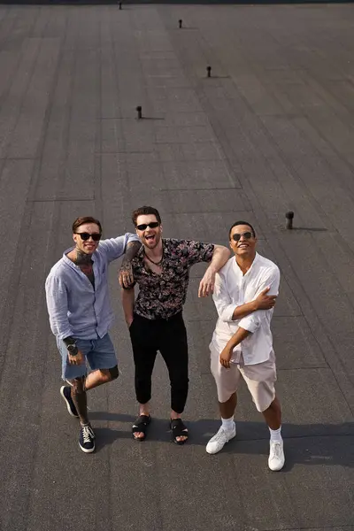 Trois amis masculins joyeux divers avec des lunettes de soleil posant sur le toit et regardant la caméra — Photo de stock