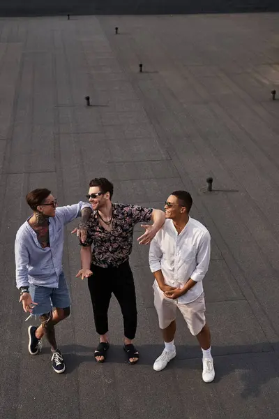Three joyous multiracial friends in vibrant attires posing on rooftop and looking at each other — Stock Photo