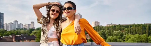 Appealing jolly women in vibrant clothes with sunglasses smiling at camera while on roof, banner — Stock Photo