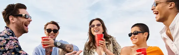 Gioiosi amici multirazziali trascorrono del tempo insieme alla festa sul tetto, bevendo dalle coppe rosse, striscione — Foto stock