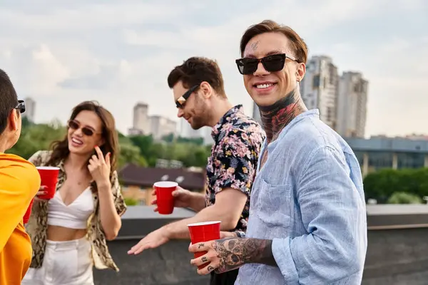 Amigos alegres atractivos con gafas de sol en trajes casuales que se divierten en la fiesta en la azotea juntos - foto de stock