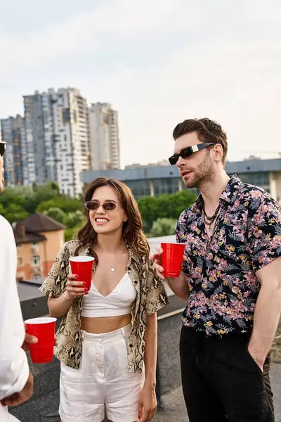Good looking jolly diverse friends with red cups with drinks talking happily at rooftop party — Stock Photo